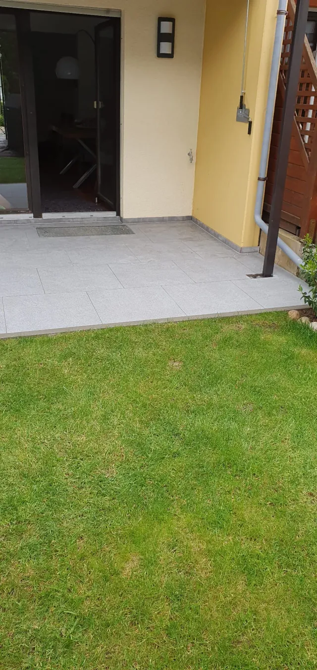 Erneuerte Terrasse mit grauen Platten und Rasen