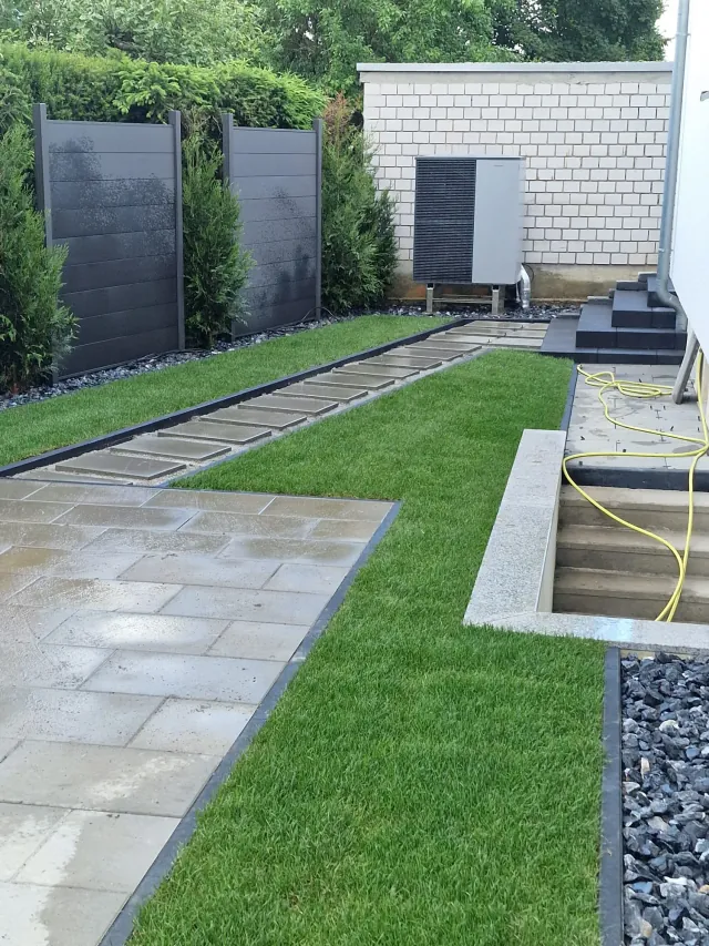 Graue Sichtschutzelemente mit Koniferen an der Grundstücksgrenze